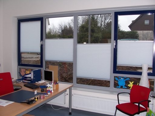 Büro mit einem Fenster, Jalousien und einem Tisch mit Computer und Stuhl.